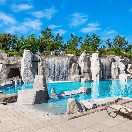 Sheraton Grande Tokyo Bay Hotel Urayasu Dış mekan fotoğraf The photo showcases a beautiful outdoor pool area surrounded by natural rock formations. There are several sand-colored stone structures, some of which feature water cascading down them, creating small waterfalls. The crystal-clear water of the pool 