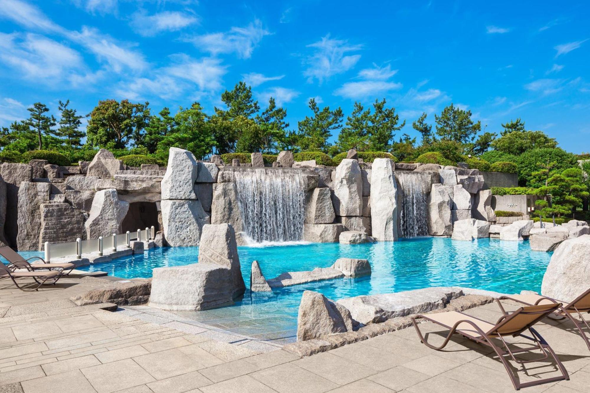Sheraton Grande Tokyo Bay Hotel Urayasu Dış mekan fotoğraf The photo showcases a beautiful outdoor pool area surrounded by natural rock formations. There are several sand-colored stone structures, some of which feature water cascading down them, creating small waterfalls. The crystal-clear water of the pool 