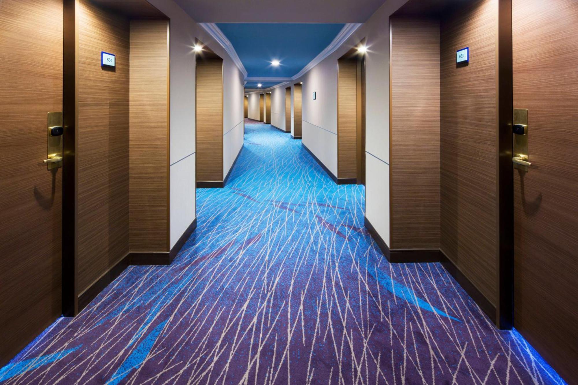 Sheraton Grande Tokyo Bay Hotel Urayasu Dış mekan fotoğraf The photo shows a hotel corridor with a stylish design. The floor features a patterned carpet in shades of blue and purple, creating a modern look. The walls are light brown with a smooth texture, and there are several doors along the corridor, each 